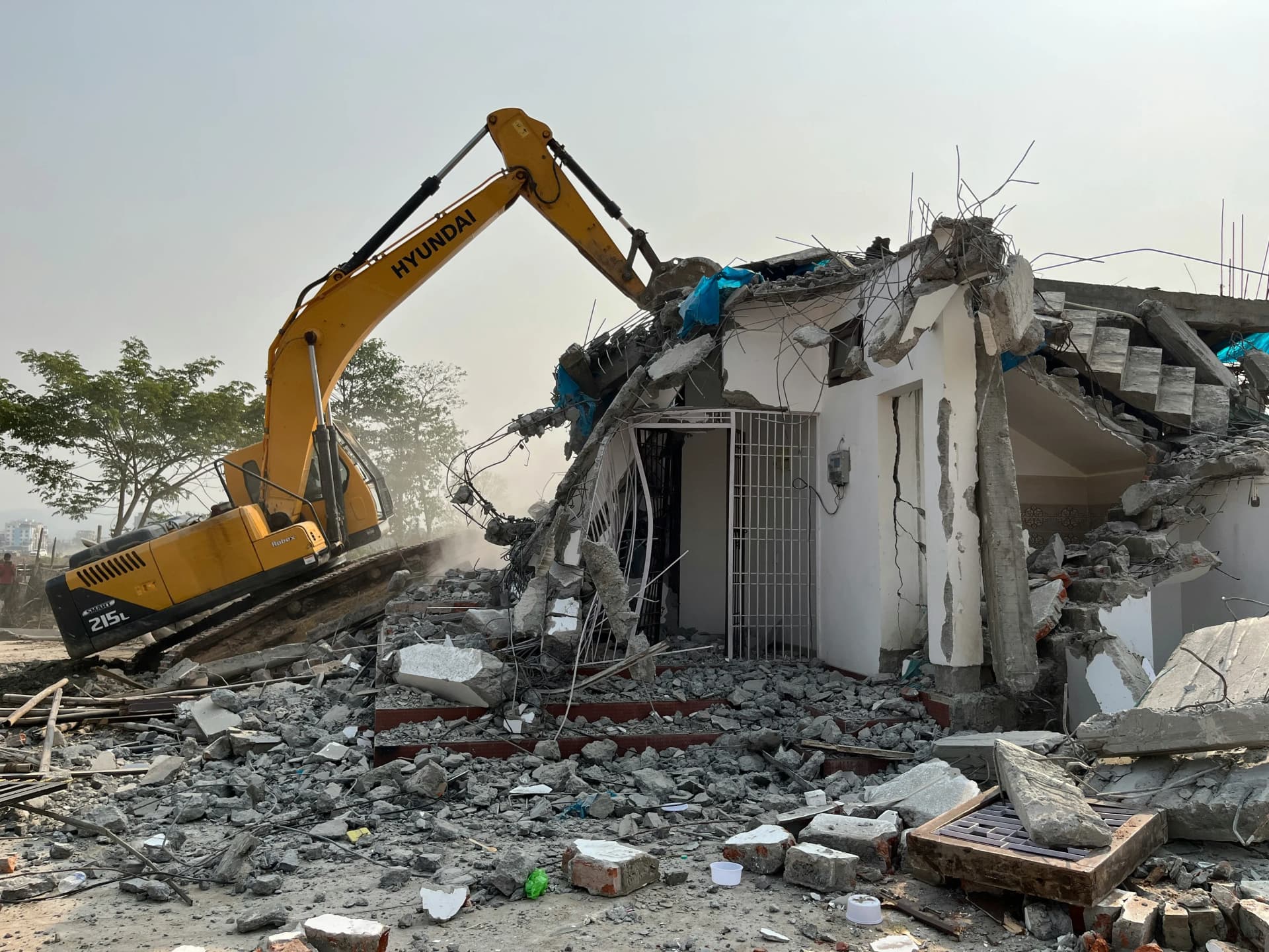 Demolition contractors carrying out concrete building demolition with a hydraulic excavator at an industrial site.